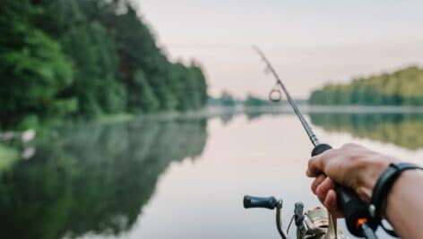 Fisherman with rod, spinning reel on the river bank. Sunrise. Fishing for pike, perch, carp. Fog against the backdrop of lake. background Misty morning. wild nature. The concept of a rural getaway. SOBOLEVSKYI.COM