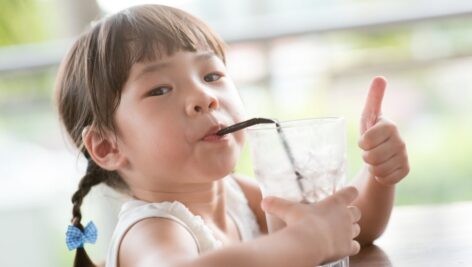 Little girl drinking water out of cup with a straw.