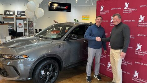 two men standing in front of gwynedd Mercy backdrop next to car