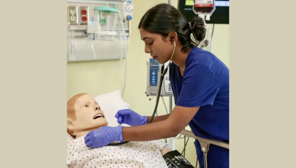 Nursing Aide Student in scrubs practicing care on a dummy.