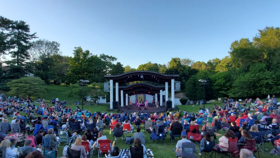 A crowd sits on the grass enjoying a performance at Delaware County's Summer Festival at the Rose Tree Park Amphitheater.