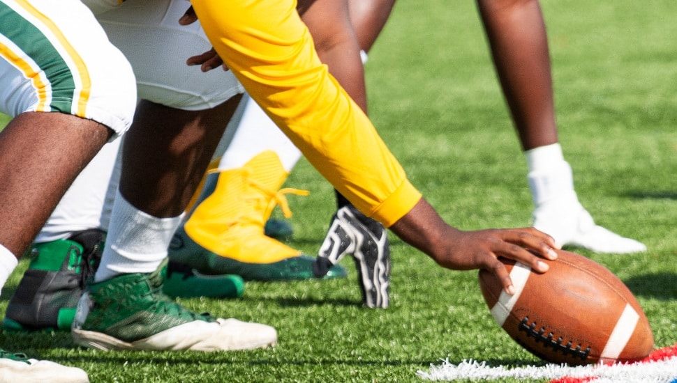 Description A high school football center is lined up and ready to snap the ball to start the play.