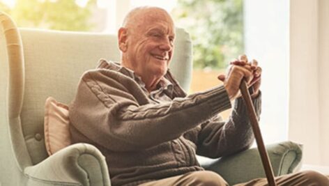 A smiling older gentleman with a cane sitting in a chair.