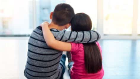 siblings putting arms around eachother, sitting on floor looking out window