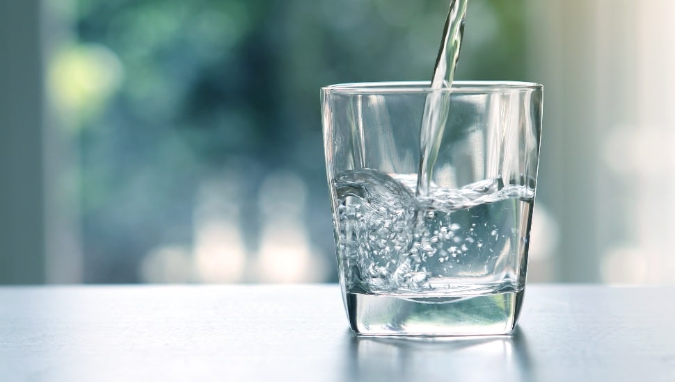 Close up pouring purified fresh drink water from the bottle on table in living room