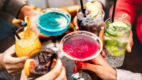 People hands toasting multicolored fancy drinks during a Happy Hour.