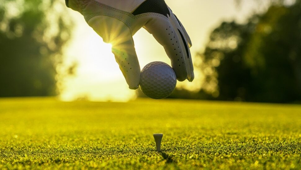 man places golf ball on tee