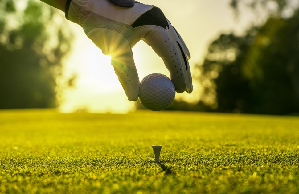 man places golf ball on tee