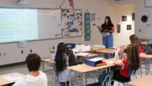 Students inside a classroom with teacher at the front of the classroom.