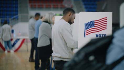 Male voter with bulletin in hands at a voting booth.