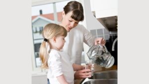 Small Girl in the kitchen with her mother drinking water.