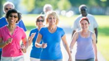 Group of older adults walking outdoors on a sunny day, smiling and enjoying a community activity in a park.