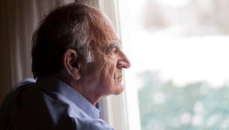 An older gentleman by a window in contemplation.