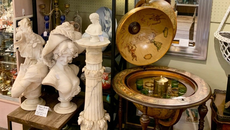 An antique globe bar and bust sculptures in an antique shop.