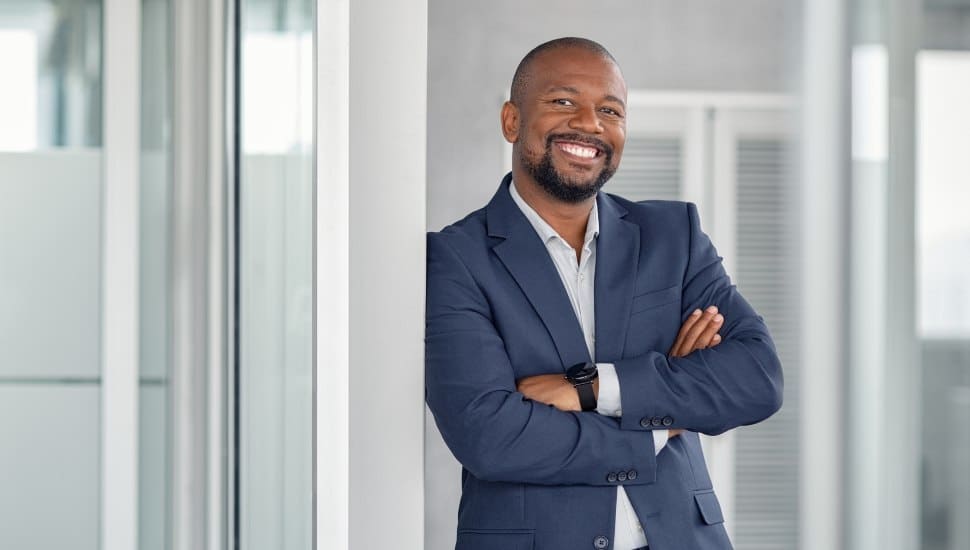 A young banking professional dressed in a suit, crossing his arms and smiling.