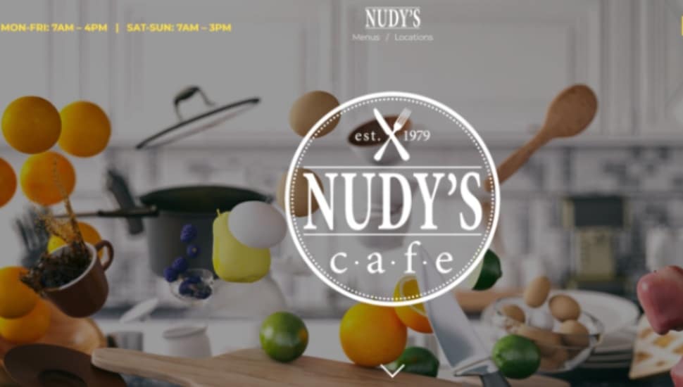 The home page of the Nudy's Cafe website showing fruit, spoons and kitchenware tossed about.
