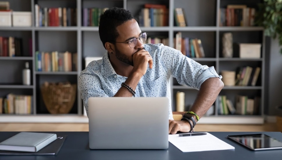 Professional sits in deep thought at a laptop computer.