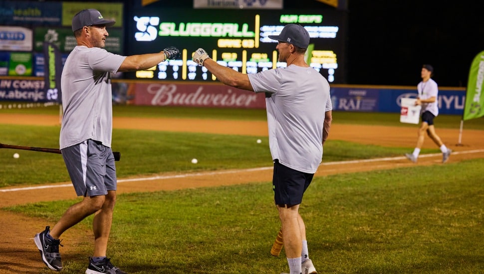 Two former baseball players bump fists on a minor league field.