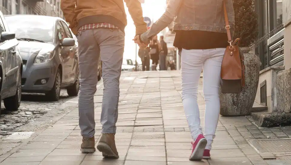 Couple holding hands and walking on a sidewalk.