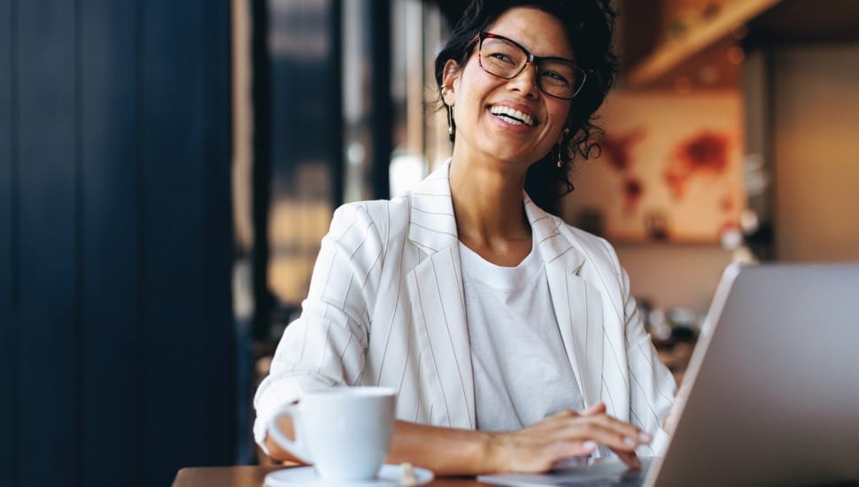 Happy businesswoman working remotely on laptop in a cozy cafe.
