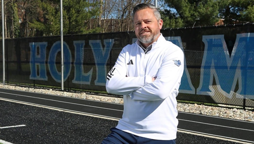 Athletic director stands with arms folded in front of university signage.