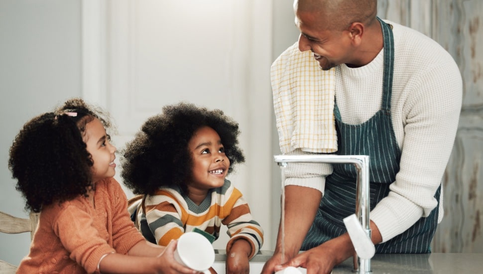 Father at kitchen sink with two little girls cleaning dishes.
