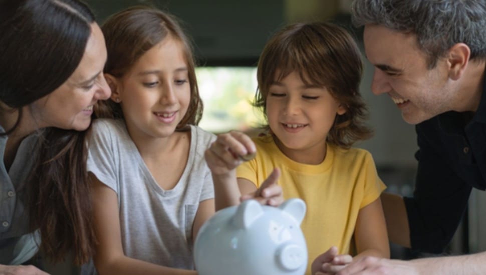 Mother and father huddle around a piggy bank with their two kids.