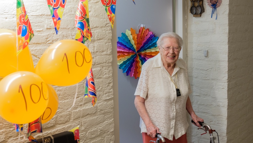 A senior woman with a walker surrounded by ballons with "100" on them.