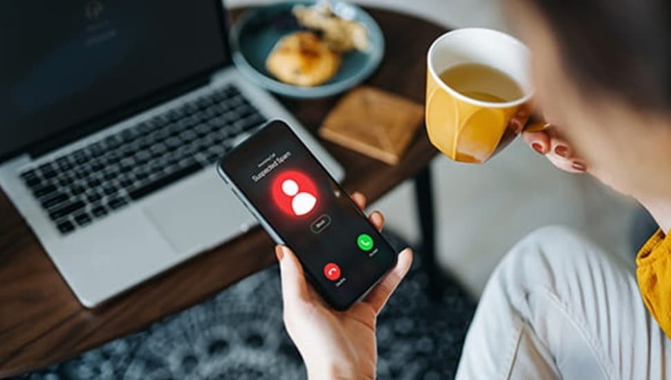 Person holding a cup of coffee picks up a ringing phone.