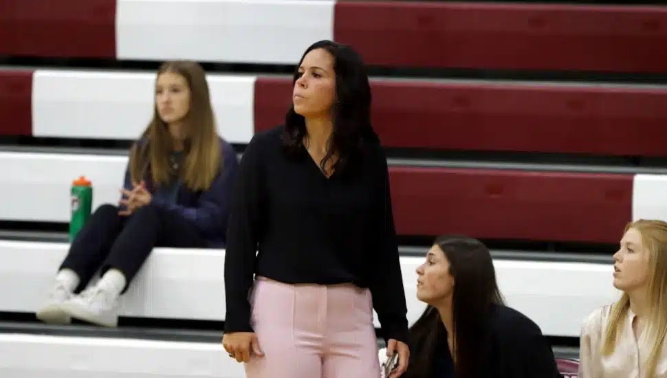 Jessica Hartzell standing on the sidelines with players sitting on the bleachers behind her.