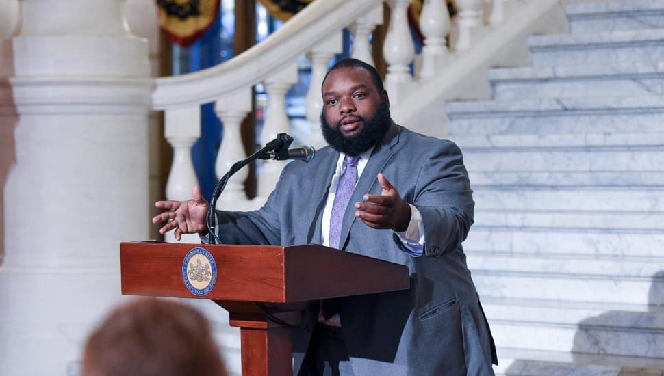 Photo of Rep. Jordan A. Harris speaking behind a podium with arms spread.