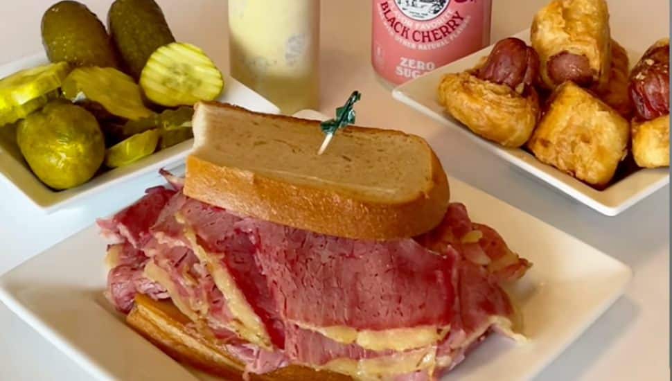 A pastrami sandwich with a side of pickles.