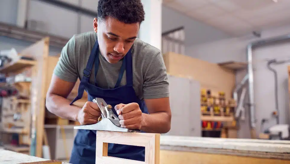 Male Student Studying For Carpentry Apprenticeship Using Wood