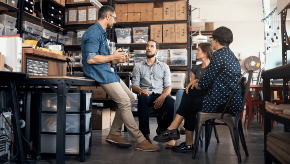 Employees sit in circle and discuss business.