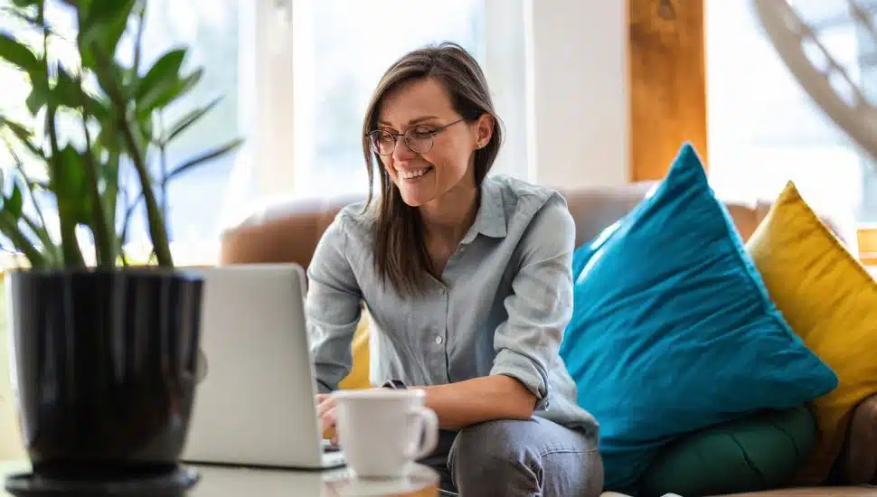 A woman sitting in her living room with her laptop and coffee.