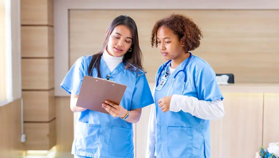 Two female nurses confer with one looking at a chart.
