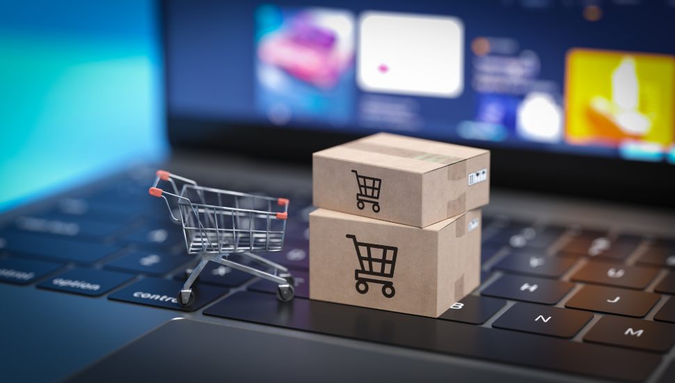 Tiny boxes and shopping cart on a laptop to represent online shopping.
