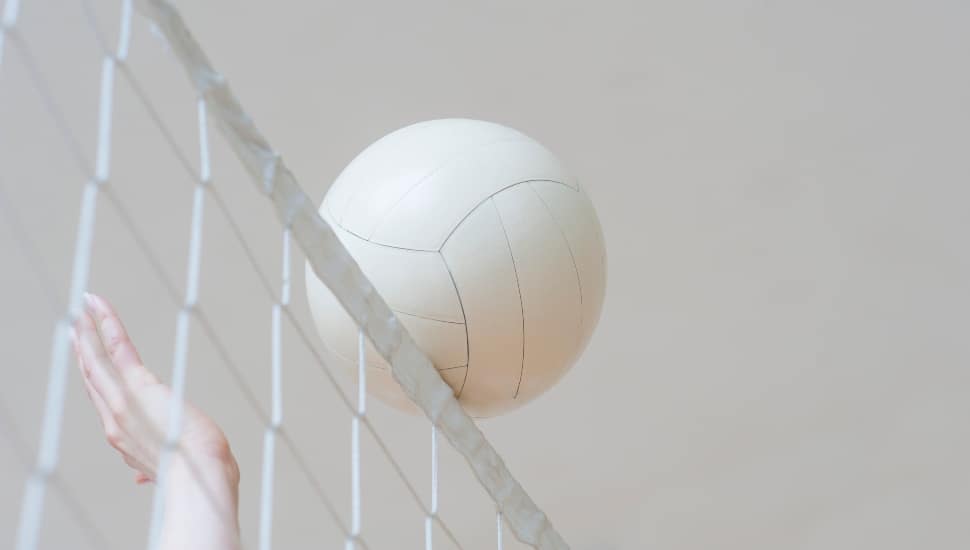 A hand reaches up to hit a volleyballl that is cresting the net.