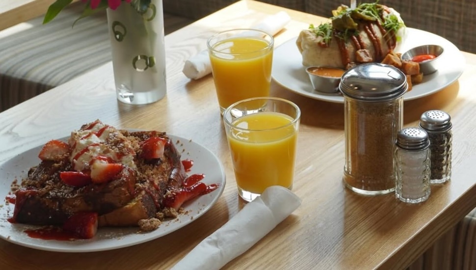Two plates of food with two glasses of orange juice and a salt and pepper shaker.