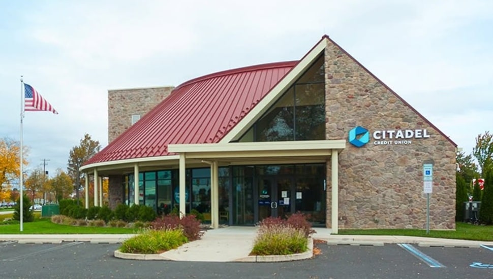 Exterior view of bank with red roof and brown stone.