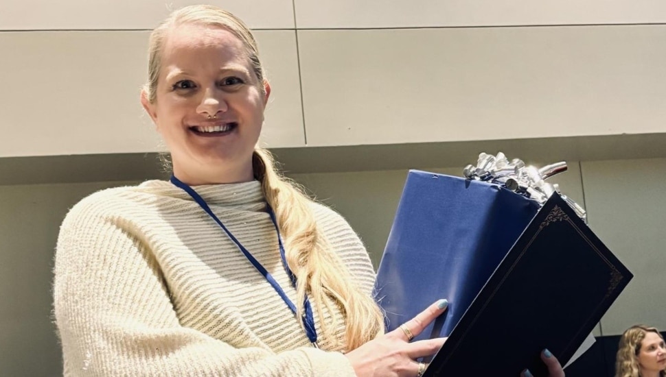 Young female nurse with blond hair and white sweater receives award.