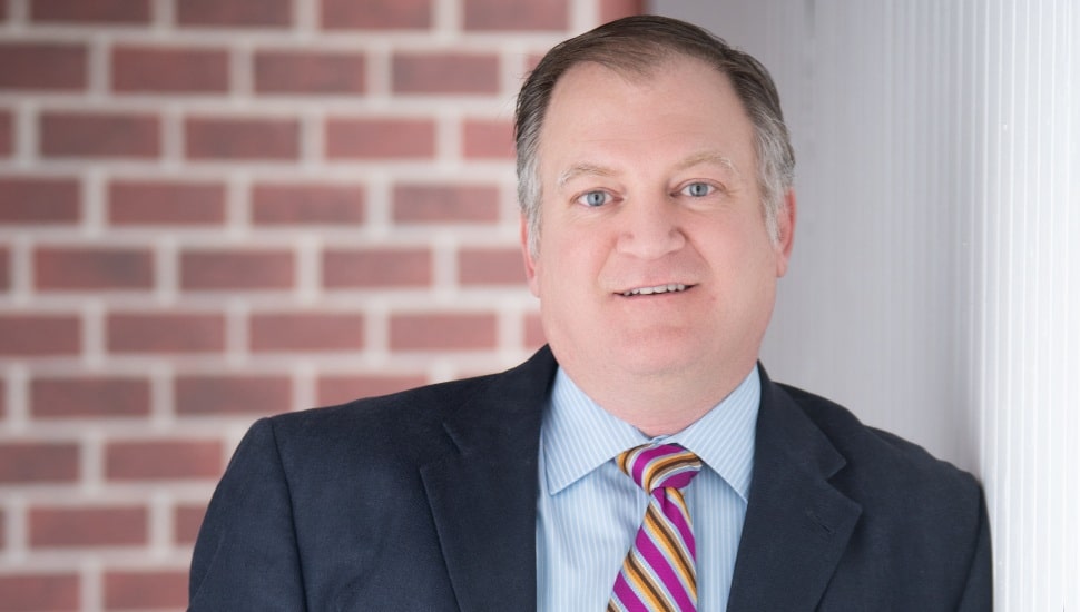 Headshot of middle-aged male attorney against a brick backdrop.