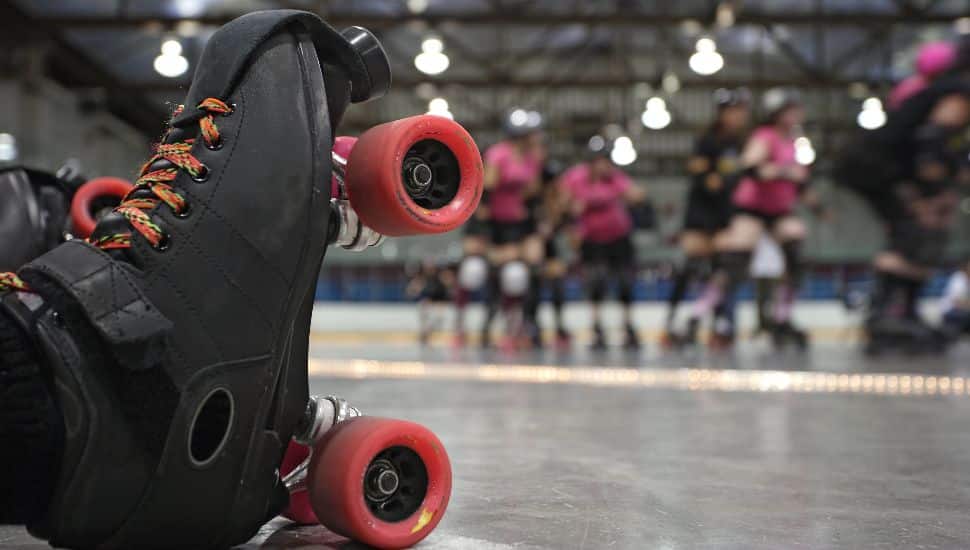 An abstract image of the roller-skates of a fallen skater as her teammates in the background continue to skate around the track of the roller derby.