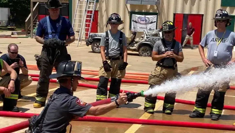 A firefighter using a hose with other firefighters in the background.