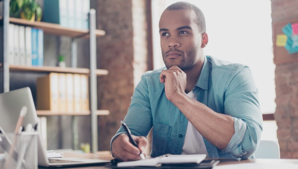 Young black male is making a decision sitting at his office desk.