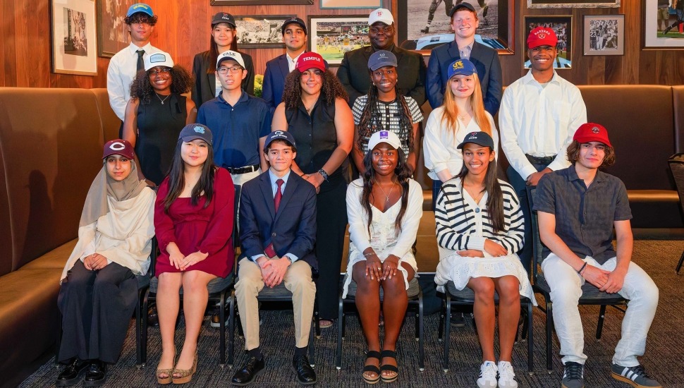 Group of high school seniors wearing hats of their college choices receive scholarships.