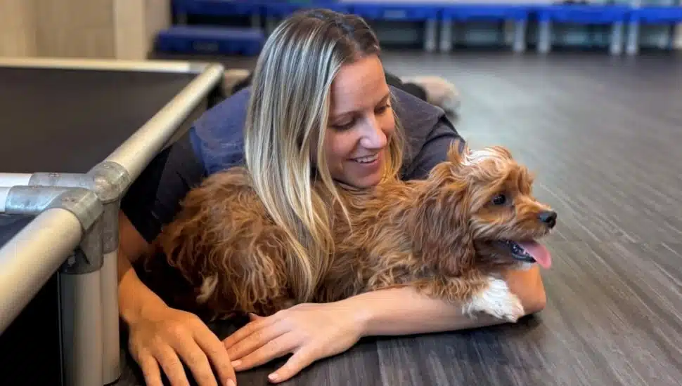 Blond woman hugs her dog while lying on the floor.