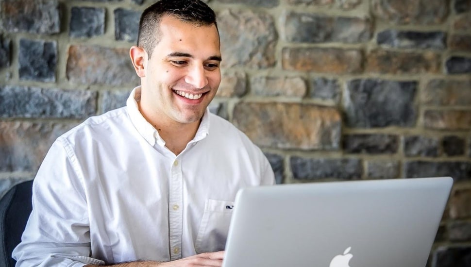 Young man in white collared shirt works on a laptop computer.