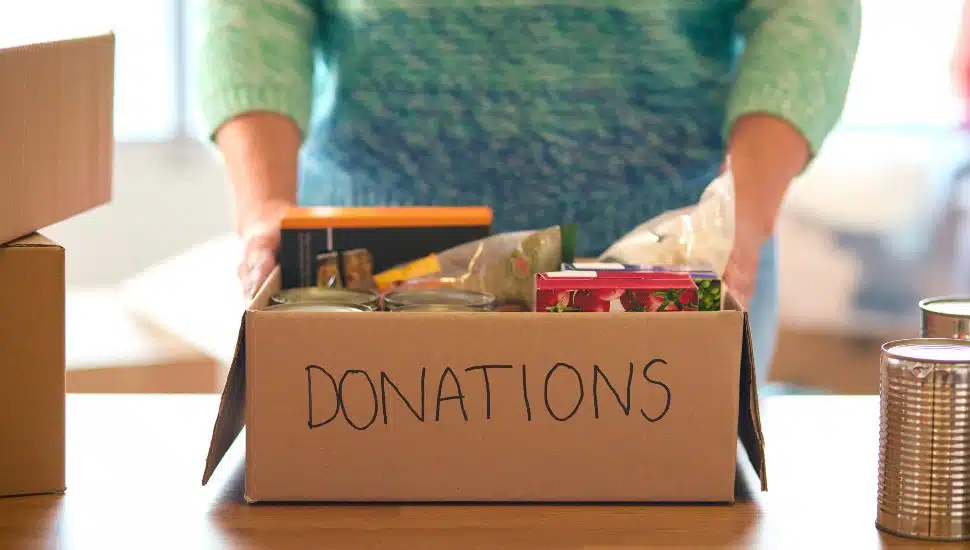 Close Up Of Female Charity Volunteer Working At Food Bank Unpacking Donations.