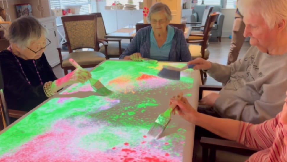Freedom Village residents work with the Happiness Program to do some virtual painting on a table.